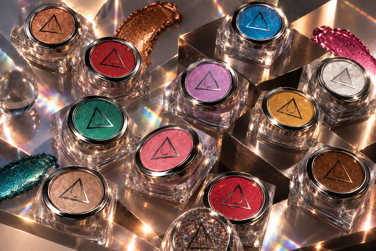 Nailspiracy chrome gel collection in clear jars with silver lids, arranged with shimmering swatches in bronze, red, blue, purple, silver, gold, teal and pink.